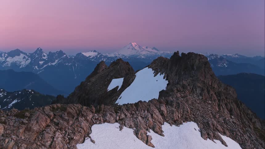 Aerial of a jagged mountain ridge as last beam of sun hits Mount Baker in distance