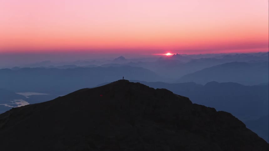 Aerial view of man on on mountain silhouetted against the red sky at sunset