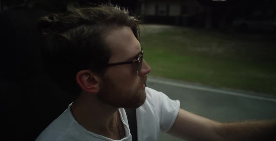 A man in a white shirt and sunglasses driving down a street