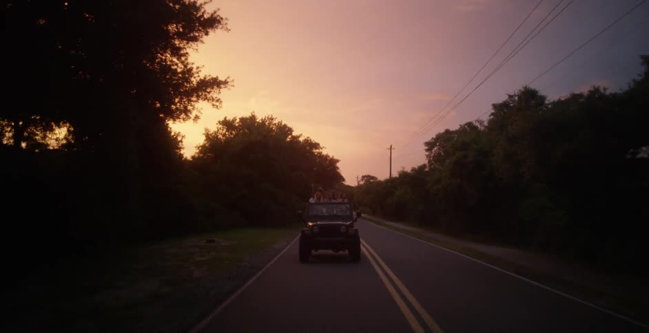 People ride down a road in a jeep with the top down, at sunset