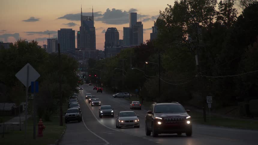 A city street with vehicles with the city skyline the sky and clouds in the background