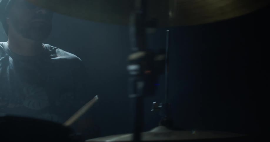 A man sits in a dark room playing the drums