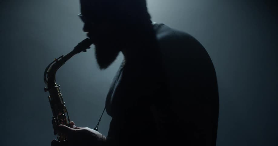A man playing a saxophone on a stage in front of a light