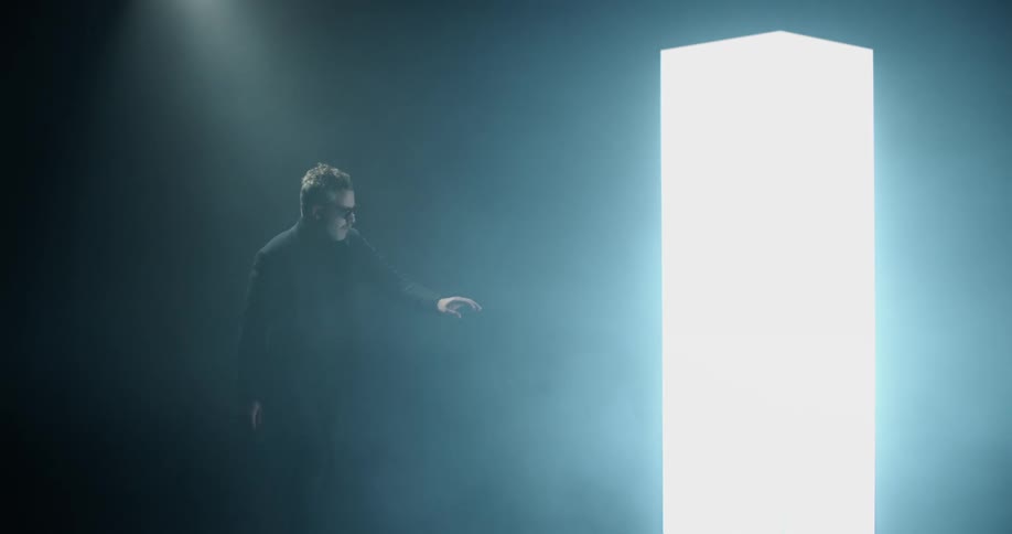 A man cautiously approaches a large glowing rectangle with his hand extended