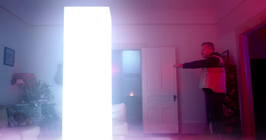 A man slowly approaches a large glowing rectangle with his arm outstretched