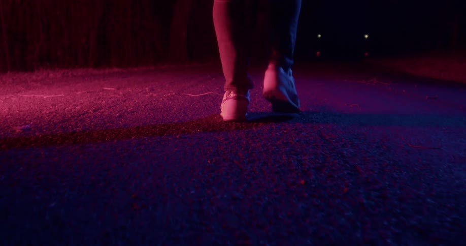 A reddish purple light shines on a person walking down the middle of a street at night