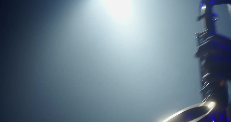 A man is playing the saxophone under the spotlight