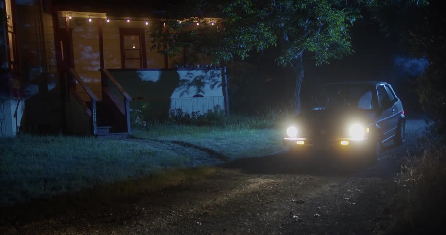 A person sits in the driveway of a rural home at night with smoke coming out of the drivers side window