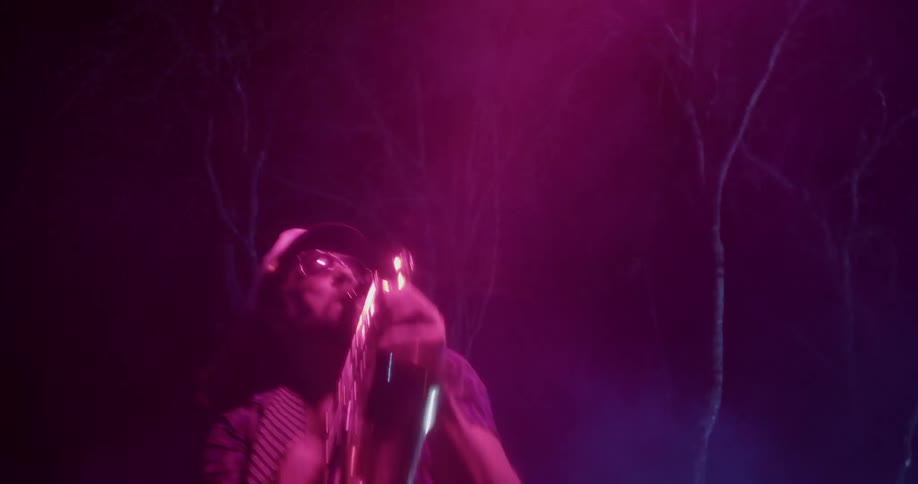 A man playing a saxophone outdoors near trees