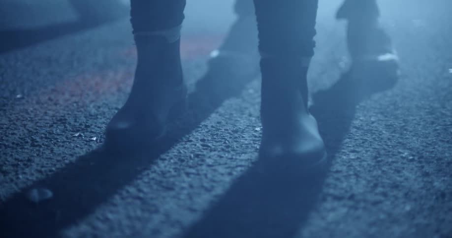 At night near parked vehicle person wearing boots backs up toward another person their shadows overlapping