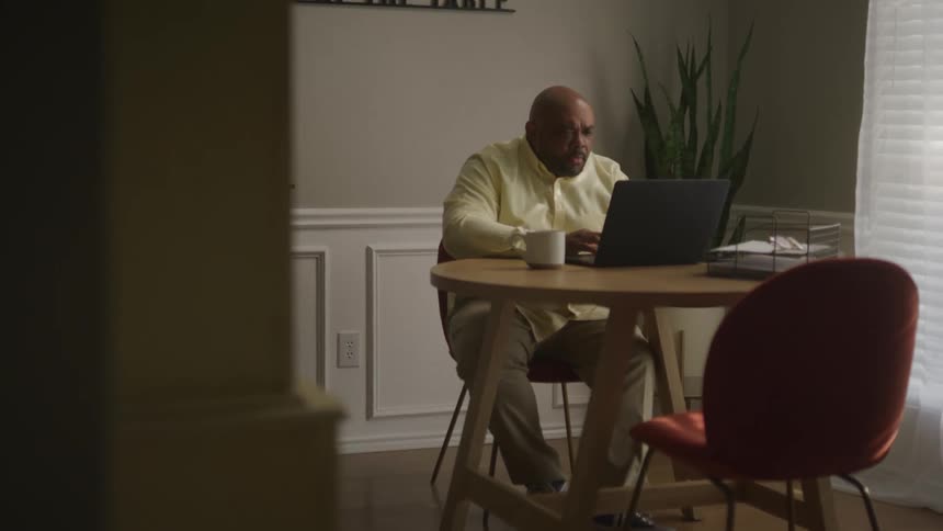 A man sits at a table while working on a laptop in front of him