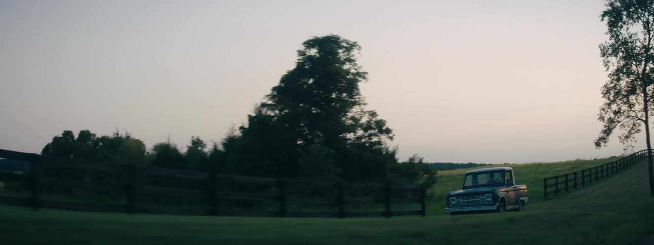 A truck travels on a country road past fences and grassy areas