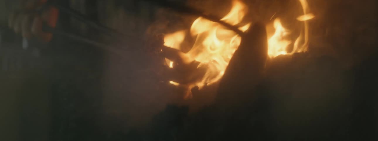 Person wearing overalls manipulates fire with metal tools
