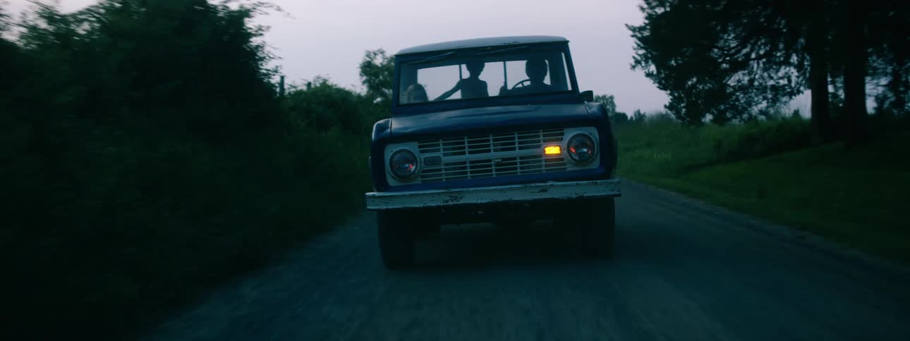 A trio of individuals are riding in an older model pickup truck on a remote road