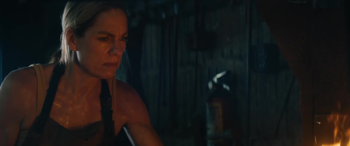 A woman with an apron in front of a furnace with a wall and fire extinguisher in the background