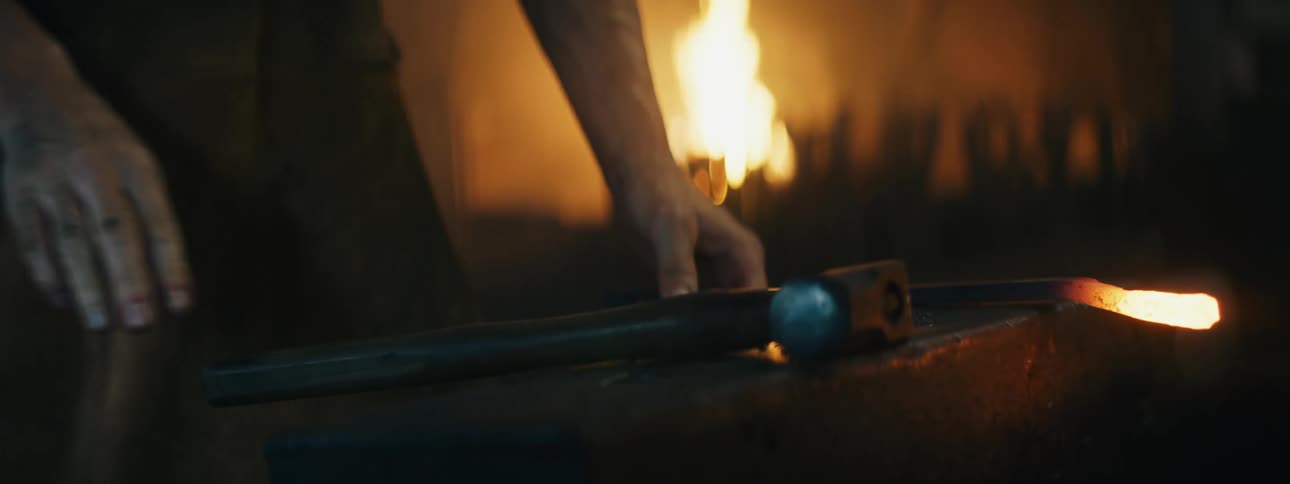 A person in a room with a hammer and anvil with a furnace and fire in the background