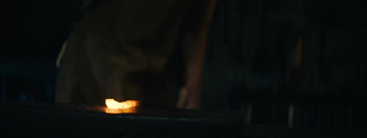 A metal worker repeatedly hammers a piece of glowing metal