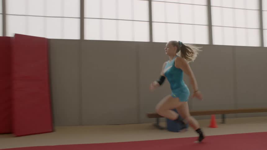 A girl runs then performs gymnastics in a gym
