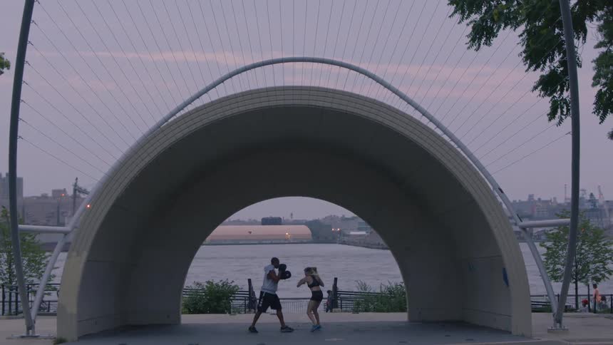 Two people practice sparring beneath a large structure