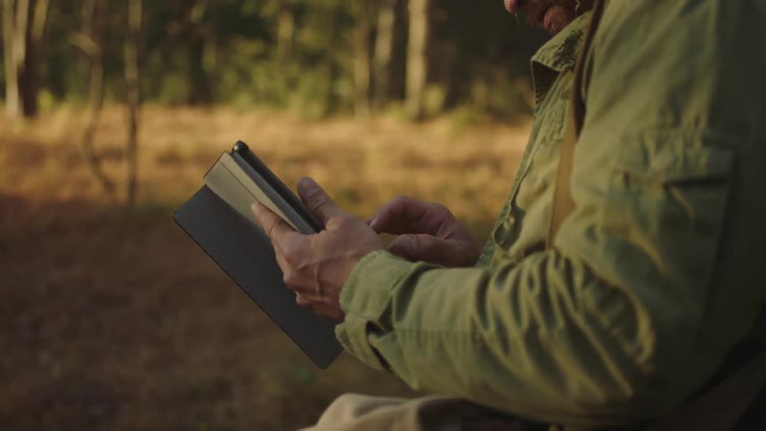 Man taps with his finger on a tablet while outside near the trees