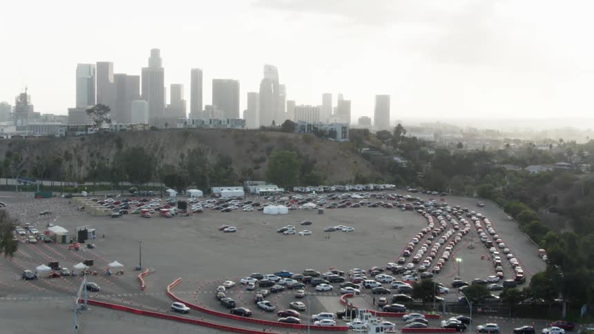 Cars wait in long lines passing through series of tents as fog shrouds city skyline