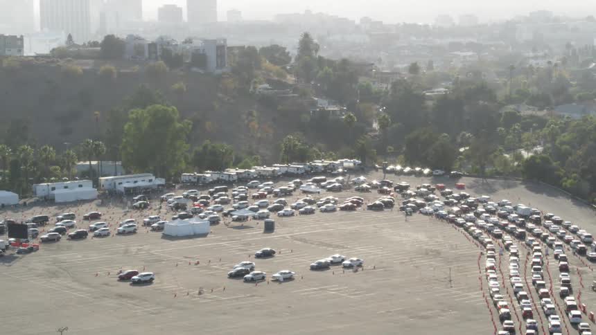 Cars slowly drive in long line ups in a parking lot with the city skyline in the distance