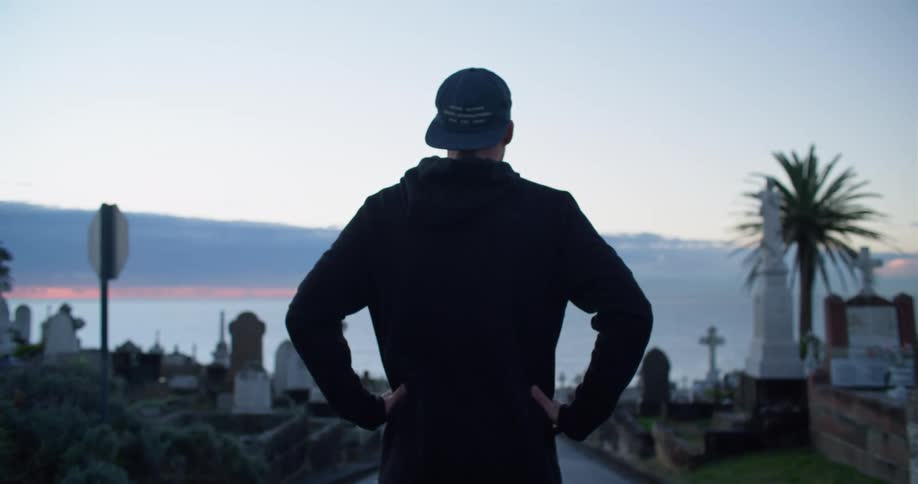 A man stands on a path that is lined with numerous cemetery headstones