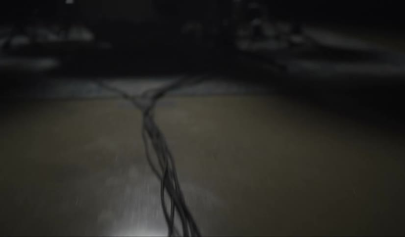 Wires along the floor leading to a drum set being played by a man in a dimly lit room