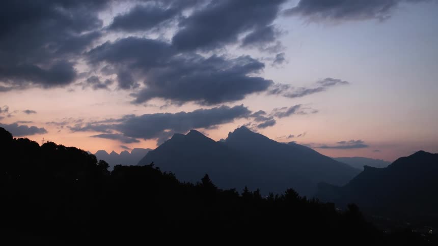 A silhouette of mountain ridge and trees with clouds overhead at dawn