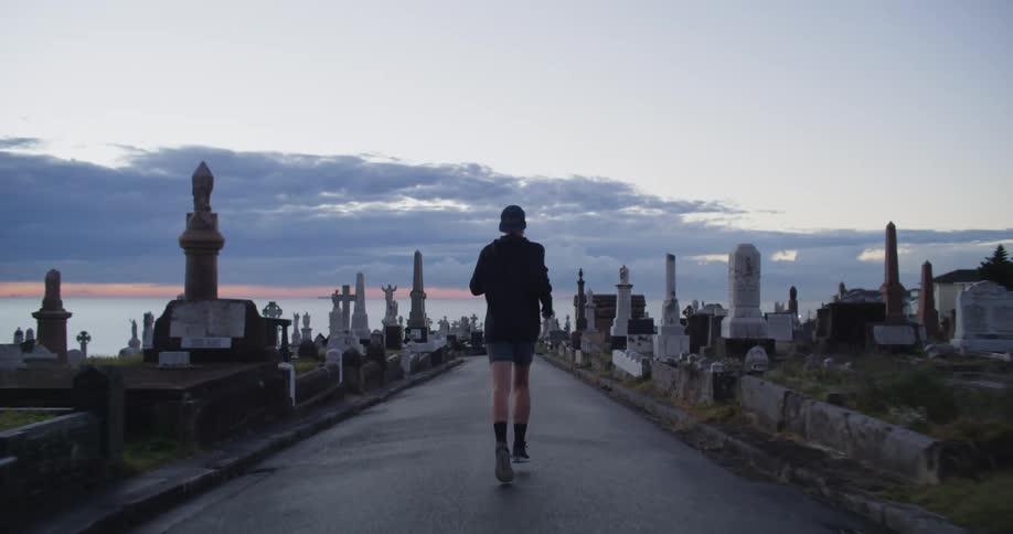 A man runs along a path next to a cemetery in front of the water