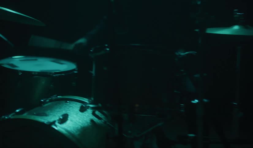 A drummer nods his head as he plays the drums in dimly lit room