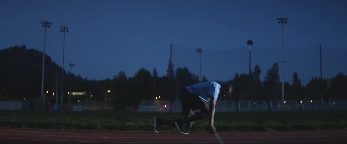 A man kneels down to start a race at night