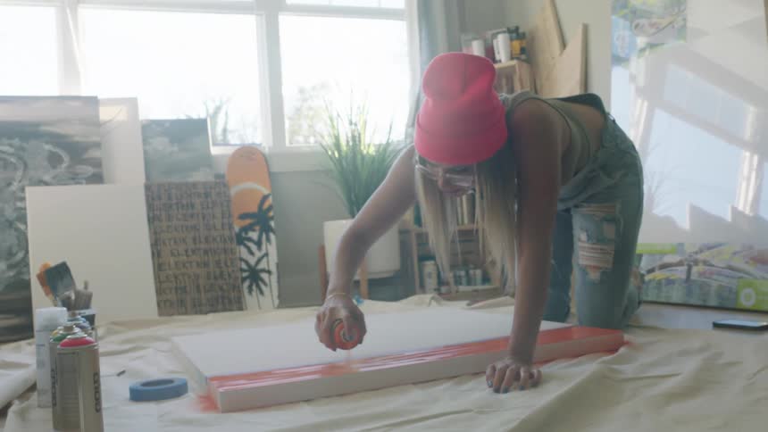 A woman spray paints a red block on a thick piece of foam board