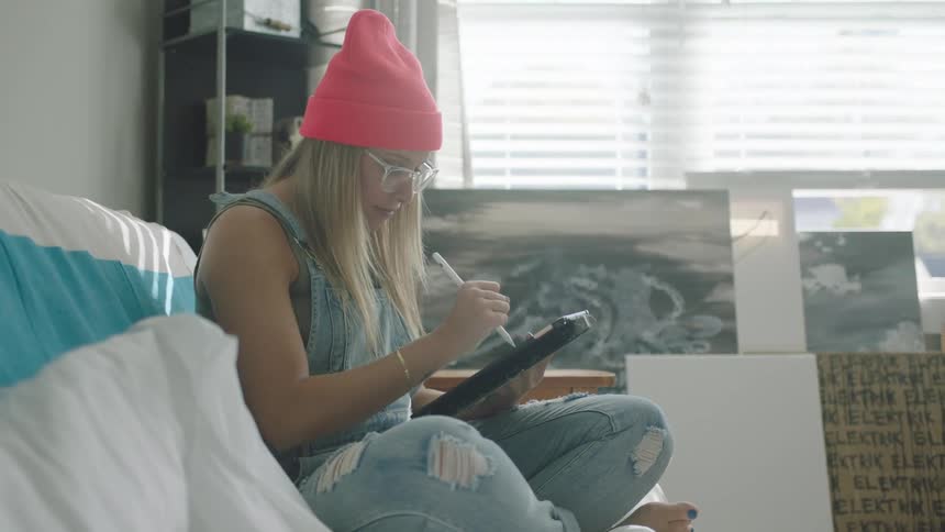 A woman in a room sitting on a couch using a tablet with a stylus