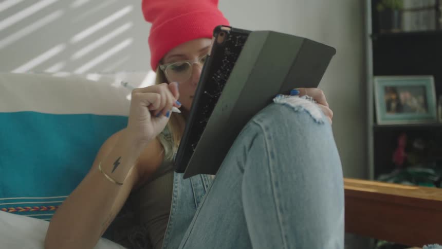 Blonde artist sitting on couch draws with stylus on tablet