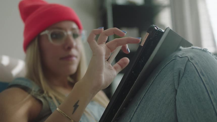 Woman wearing overalls and knit hat writes on convertible laptop with stylus