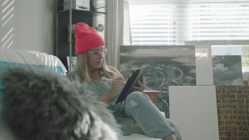 A woman is sitting on a couch and using a tablet