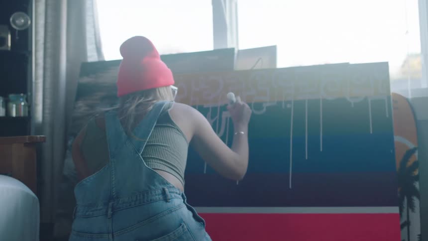 A woman in a room painting on a canvas with a window in the background