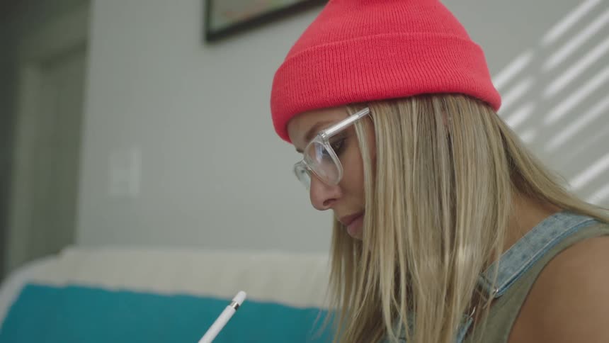 Blonde woman sits on couch drawing on tablet with stylus
