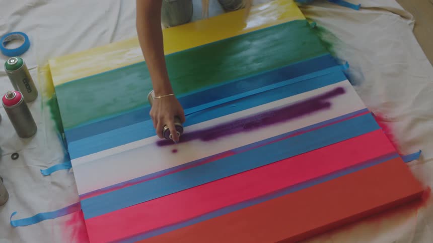 A woman in a room on the floor spray painting on a canvas