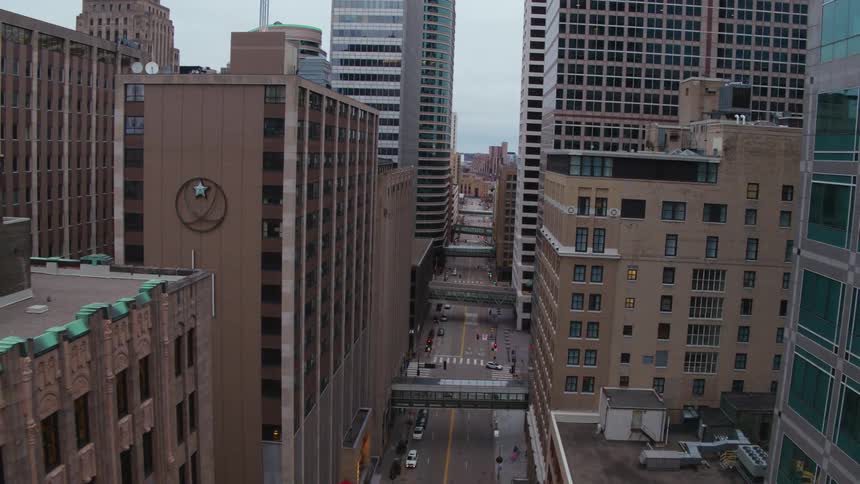 Cars travel on a city street between buildings downtown