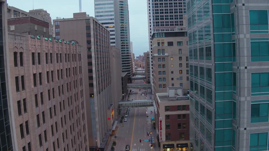 A city street with vehicles surrounded by buildings with the sky and clouds in the background