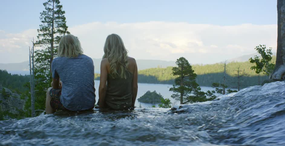 Man and woman sit near a waterfall under a cloudy sky