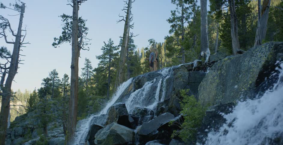 A man and woman are standing at the top of a waterfall during the day