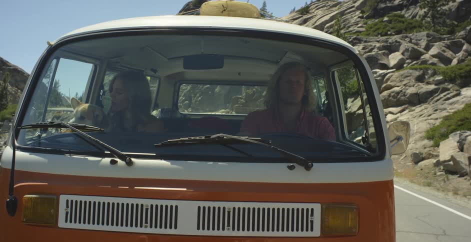 A man and woman are riding down the road in an old van