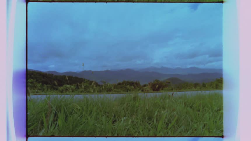 A grassy floodplain near a river, with mountains and clouds ahead