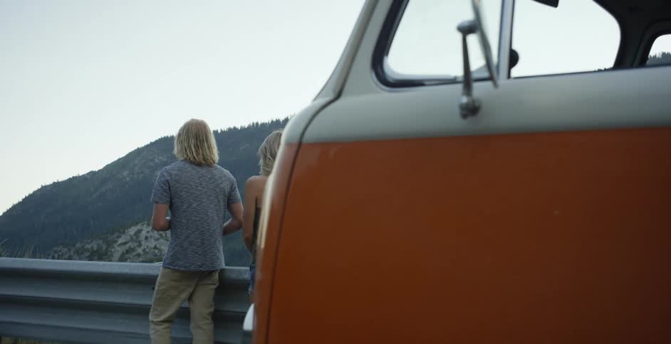 A man and woman are stopped on the side of the road looking out over the valley