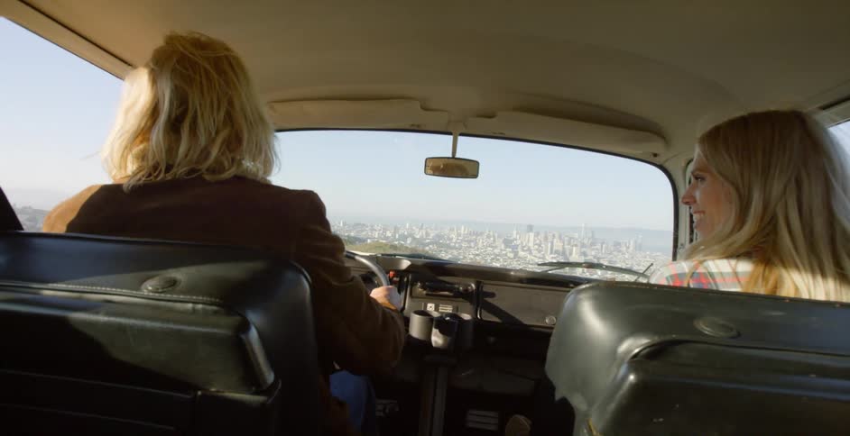 A man and woman are driving in a v.w. bus outside of los angeles on a sunny day