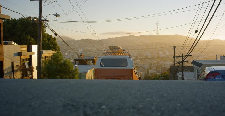 Volkswagen bus drives on a city street at sunset