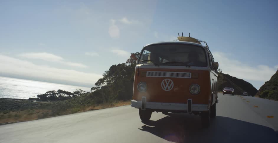 A volkswagen bus drives on a coastal road